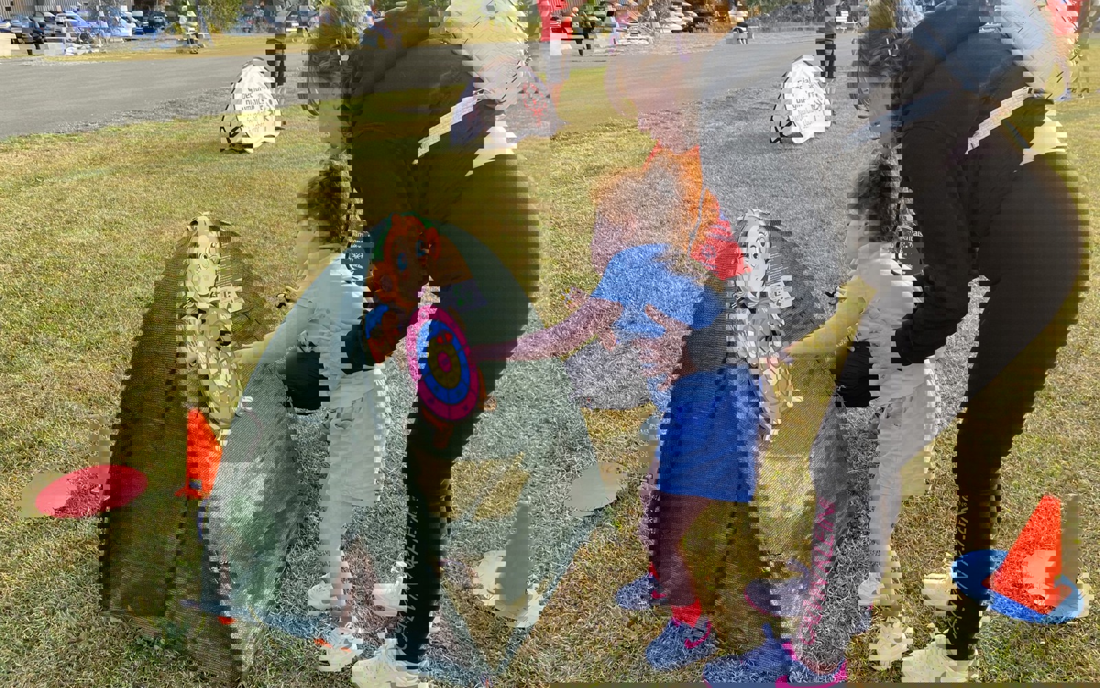 Photo taken outdoors. A little girl, being supported by her mother, is playing with a pop up toy. 