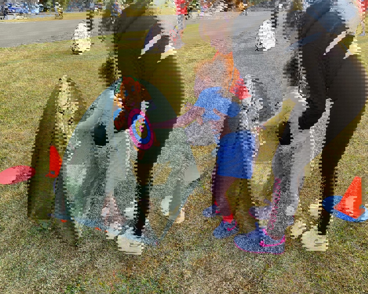 Photo taken outdoors. A little girl, being supported by her mother, is playing with a pop up toy. 